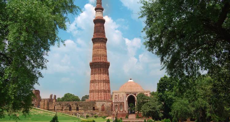 Qutub Minar mit umliegenden Grünflächen unter blauem Himmel.