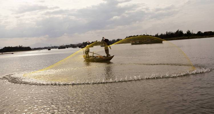 Fisherman casting a net into the water from a small boat.