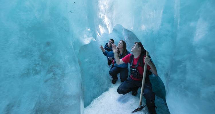 Gruppe von Menschen, die das Innere einer blauen Eishöhle erkunden.