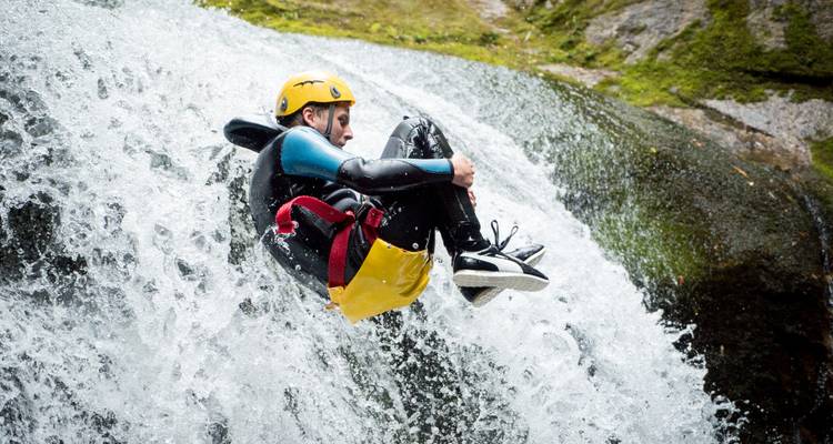 Person in einem Neoprenanzug, die einen Wasserfall hinunterrutscht.
