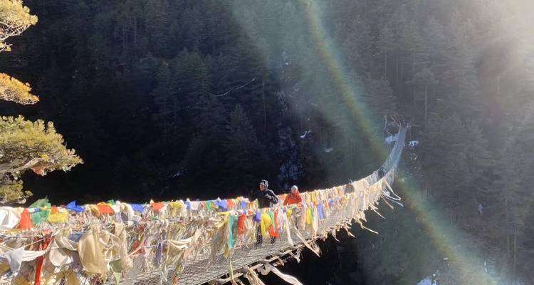Zwei Personen überqueren eine Hängebrücke mit Gebetsfahnen.