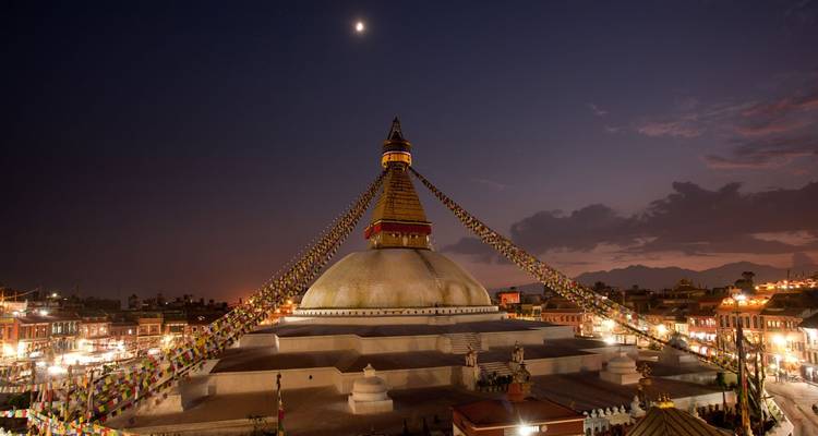Eine große Stupa mit Gebetsfahnen unter einem strahlenden mondbeschienenen Himmel.
