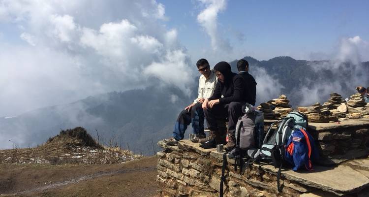 Three hikers resting on a stone outcrop with a foggy mountain view.