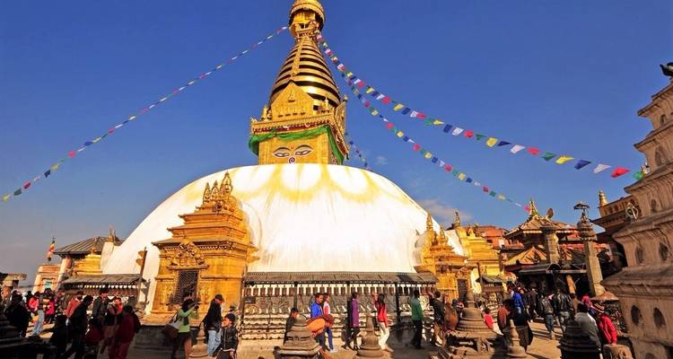 Eine große Stupa mit bunten Gebetsfahnen und Menschen drum herum.