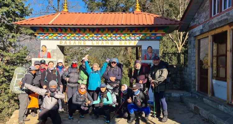 Un gran grupo de trekking se reúne en la entrada del sendero Pasang Lhamu Gate bajo un cielo azul despejado.