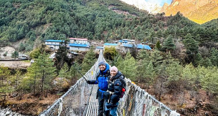Dos trekeros cruzan un largo puente colgante sobre un valle cubierto de bosque en Nepal.