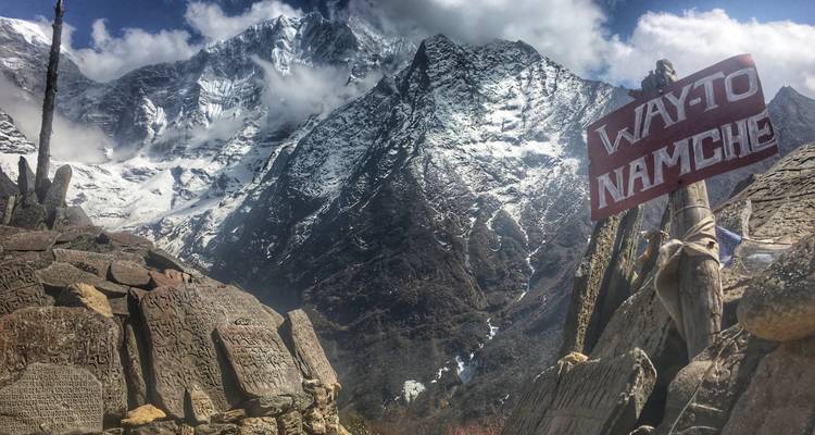 Señalización del camino a Namche con tallados detallados de montañas en una zona montañosa.