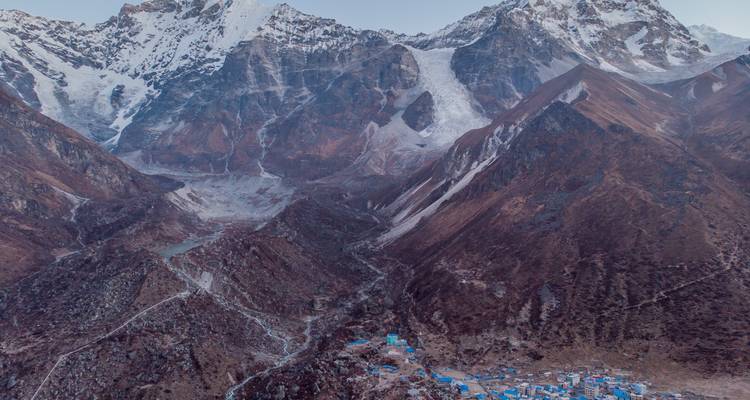 Un village niché dans une vallée de montagne avec des sommets enneigés tout autour.