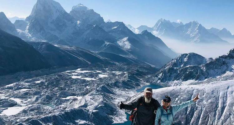 Dos personas posando en una ubicación de gran altitud con montañas nevadas.