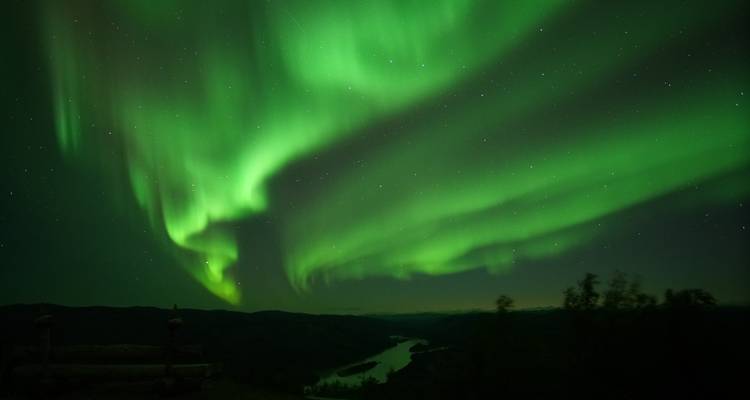Aurores boréales vibrantes illuminant le ciel au-dessus d'un paysage fluvial.