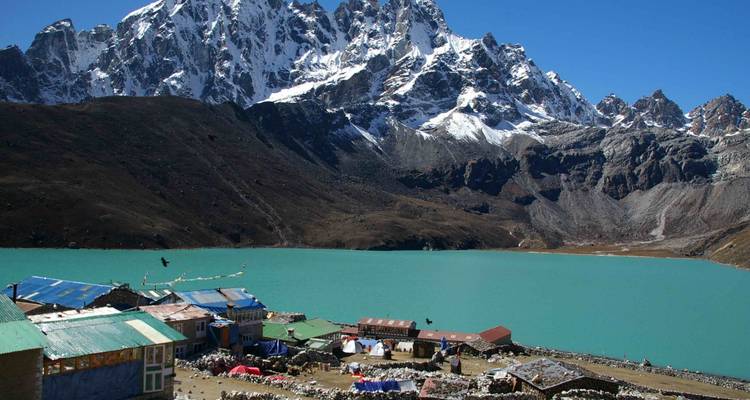 Türkisfarbener See mit umliegenden Gebäuden und schneebedeckten Bergen.