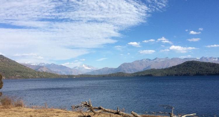 See mit Treibholz und Bergen im Hintergrund