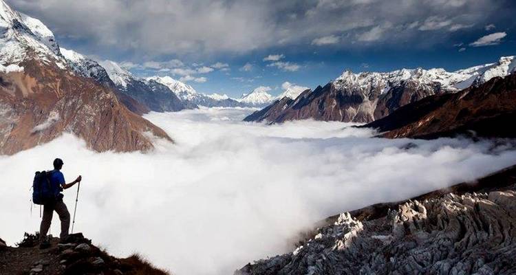 Wandelaar die boven een dal staat gevuld met wolken, omringd door bergen.