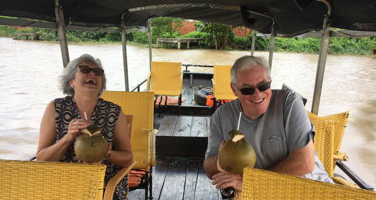 Älteres Paar lacht mit tropischen Getränken in der Hand auf einem Boot.