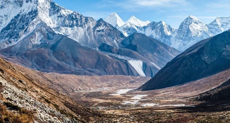 Wide valley surrounded by snow-capped mountains under a clear sky.