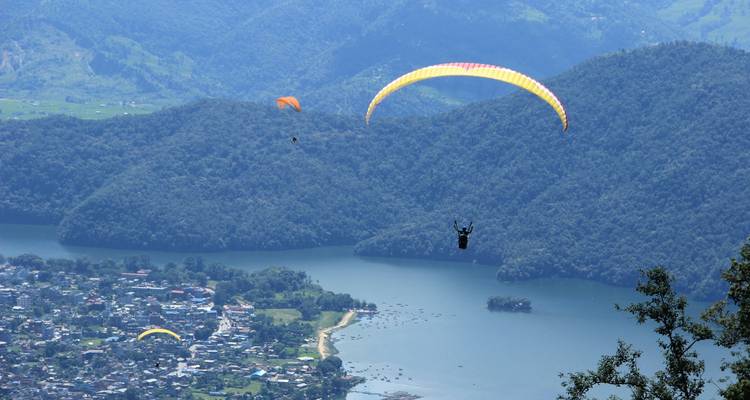 Parapentistas volando sobre un lago y montañas en Pokhara.