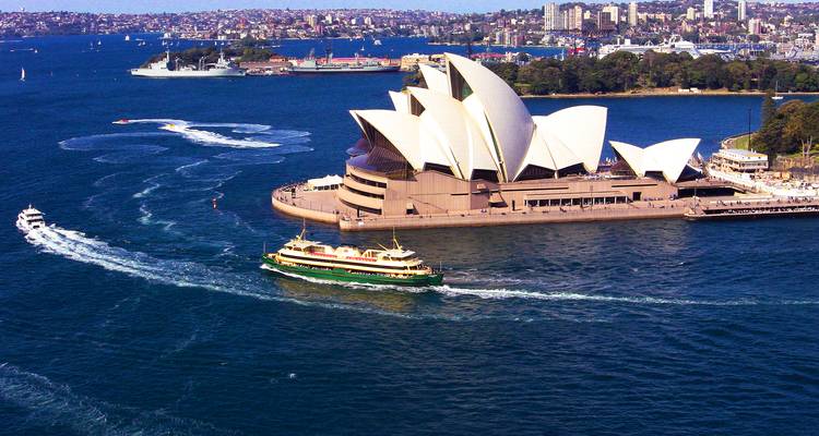 Aerial view of Sydney Opera House with ferries and deep blue harbour waters on a sunny day.