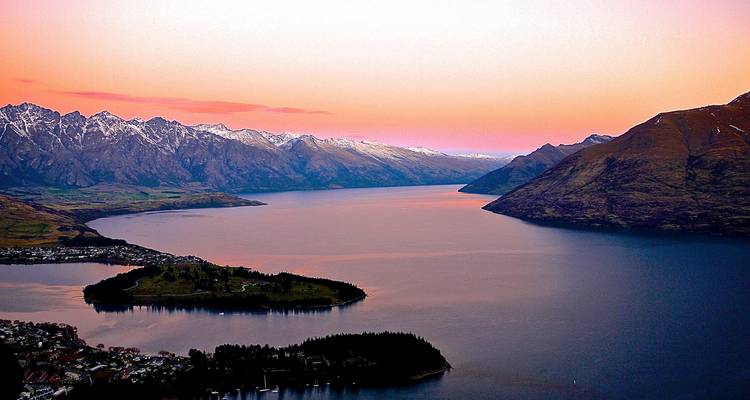 Twilight view over Lake Wakatipu with snow-capped Remarkables and glowing pink sky near Queenstown.