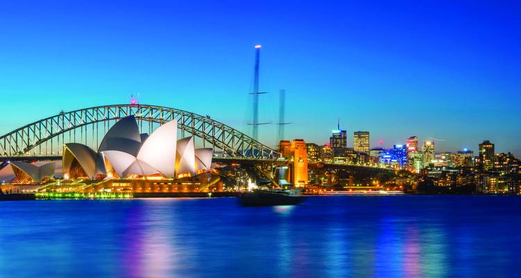 Sydney Opera House and Harbour Bridge illuminated over shimmering blue harbour at twilight.