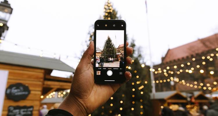 Gros plan d'un écran de smartphone capturant un sapin de Noël décoré sur une place de ville.