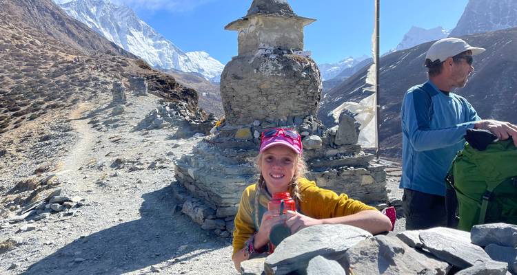A smiling trekker rests beside a stone stupa on a rugged Himalayan trail.