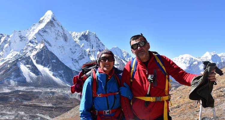 Two climbers in bright gear stand before the sharp snow-clad peak of Ama Dablam.