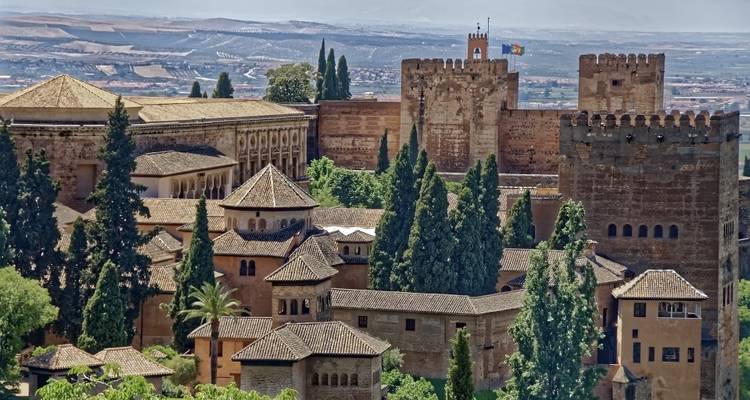 Una mirada más cercana a las torres y muros del complejo de la Alhambra rodeados de árboles de ciprés.