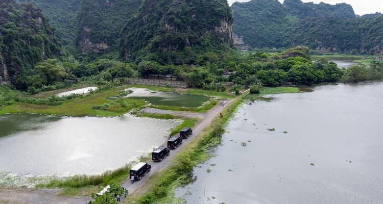 Aerial view of serene landscapes with a line of black vans on a narrow road.