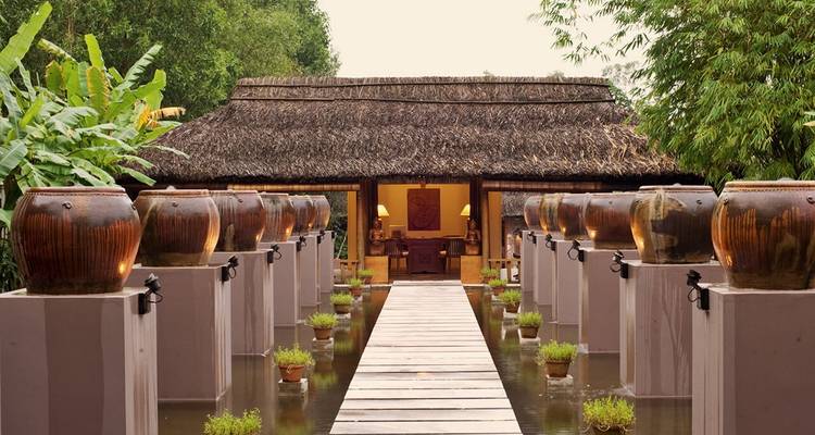 Traditional wooden house with a path lined by large vases and water features.