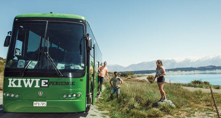 Grupo de personas junto a un autobús de Kiwi Experience con vista al lago.