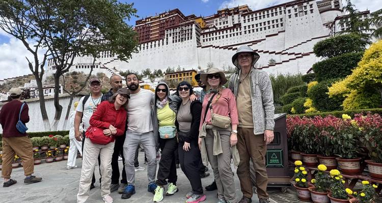 Grupo de turismo sonriendo frente al imponente Palacio de Potala blanco y rojo bajo un cielo azul