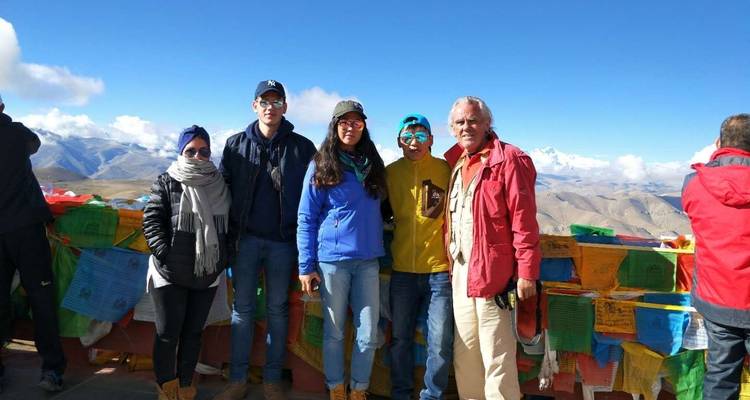 Grupo de personas posando con banderas de oración coloridas y montañas.
