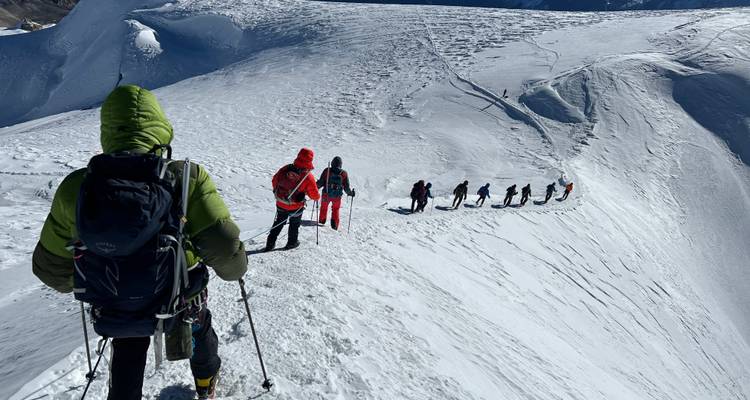 Ligne de grimpeurs progressant le long d'une crête montagneuse enneigée.