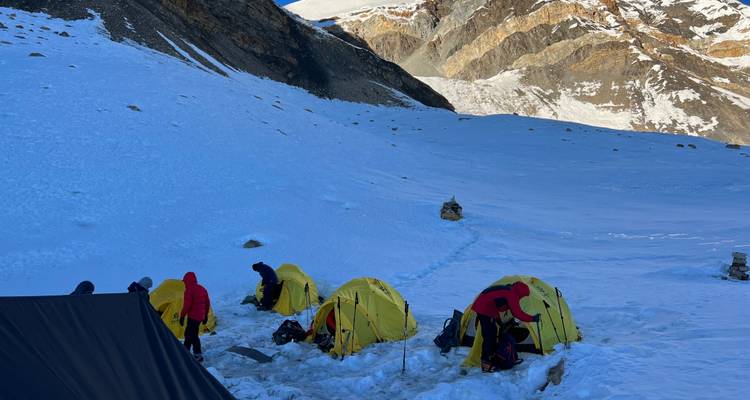 Ensemble de tentes jaunes dans une vallée de montagne enneigée.