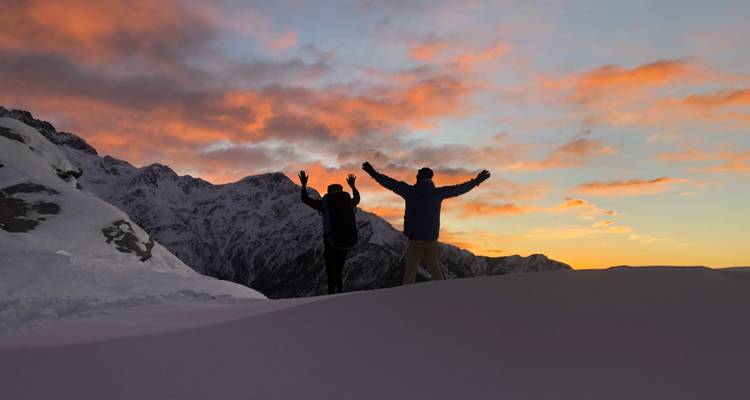 Silhouettes of people against a vibrant sunset sky on a snowy mountain.