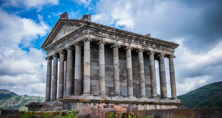 Antiker Tempel mit klassischen Säulen vor einer bergigen Kulisse.