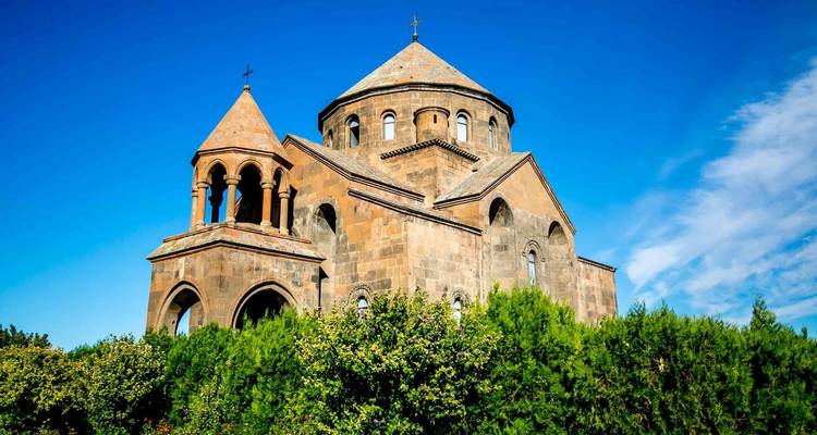Eine mittelalterliche Kirche, umgeben von üppigem Grün und einem strahlend blauen Himmel.