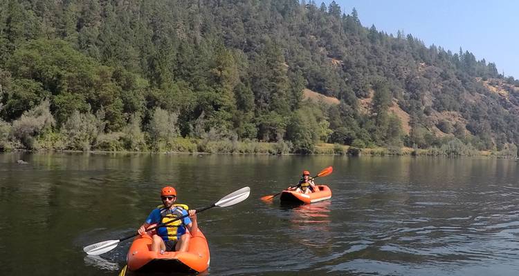 Deux personnes en kayak sur une rivière calme entourée de forêt.
