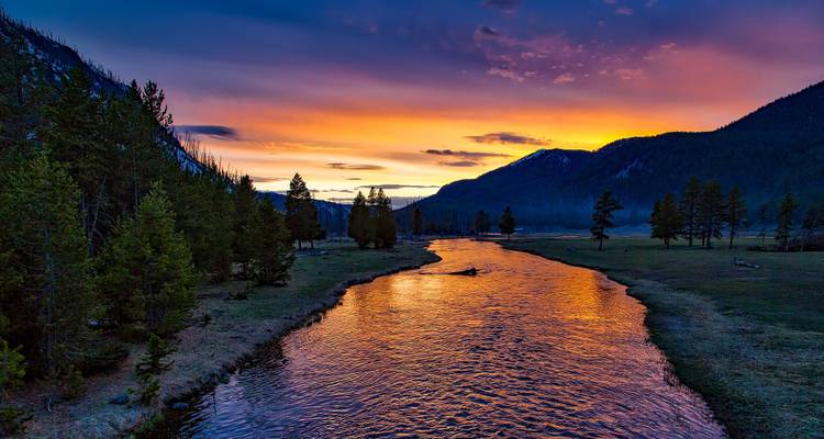 Rivière coulant à travers une vallée avec un ciel de coucher de soleil coloré.