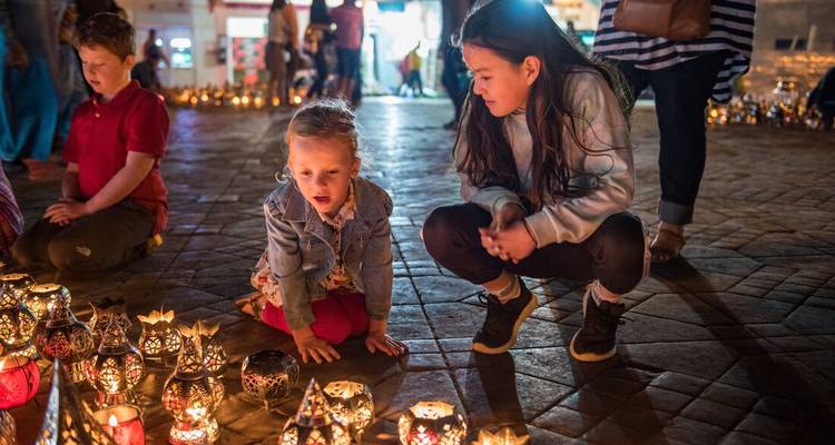 Deux jeunes filles admirent des rangées de lanternes brillantes sur une place pavée la nuit.
