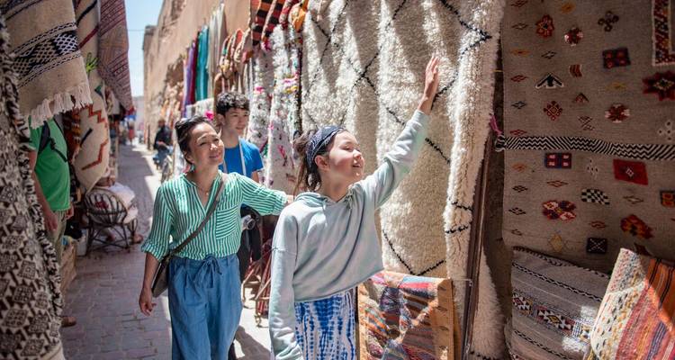 Mère et enfants parcourent des tapis colorés tissés à la main dans une ruelle animée du souk.