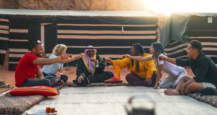 Reizigers die thee delen met Bedoeïen gastheer binnen traditionele woestijnkamp tent