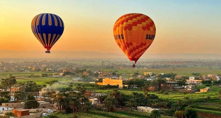 Globos aerostáticos volando sobre un paisaje verde al atardecer.