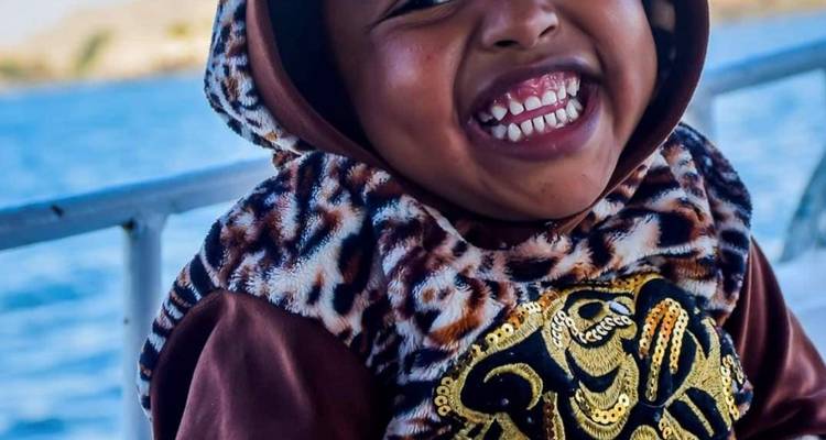 Smiling child in a patterned outfit on a boat.