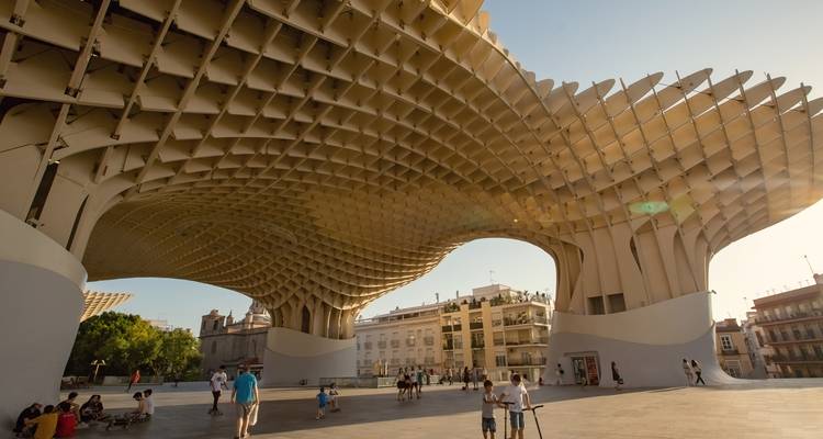 Weiter Platz unter dem geschwungenen Gitterdach von Sevillas Metropol Parasol mit Menschen, die im späten Nachmittagslicht spazieren gehen.