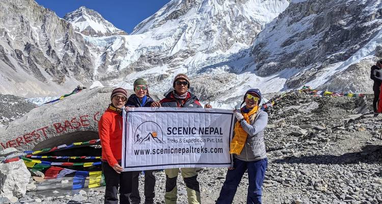 Turistas sosteniendo una pancarta frente a un letrero que dice 'Campamento Base del Everest'.