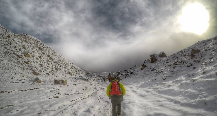Eine Person, die auf einem schneebedeckten Wanderweg unter einem bewölkten Himmel wandert.