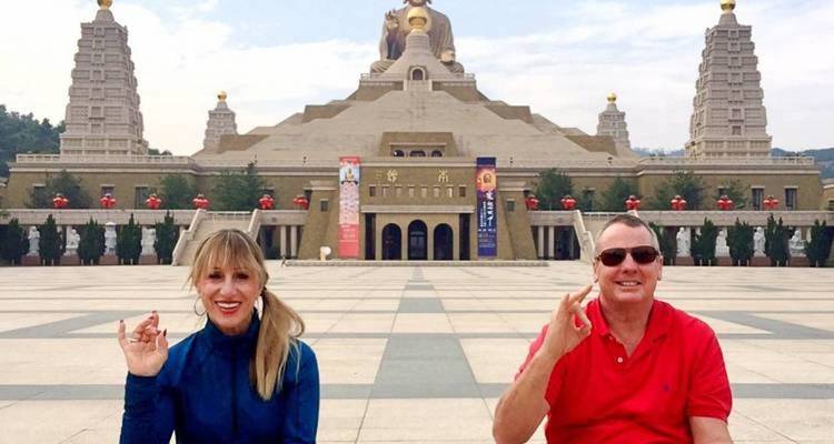 Two people posing in front of a large statue and temple complex.