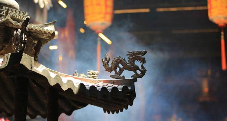 Intricate dragon sculpture on a roof with smoke and lanterns.
