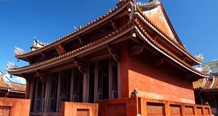 Traditional red-walled temple with intricately carved rooflines and bright blue sky background.